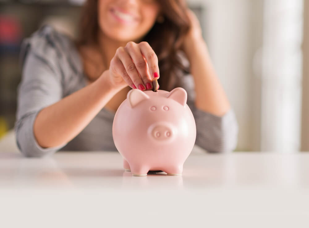 woman putting coin in pink piggy bank